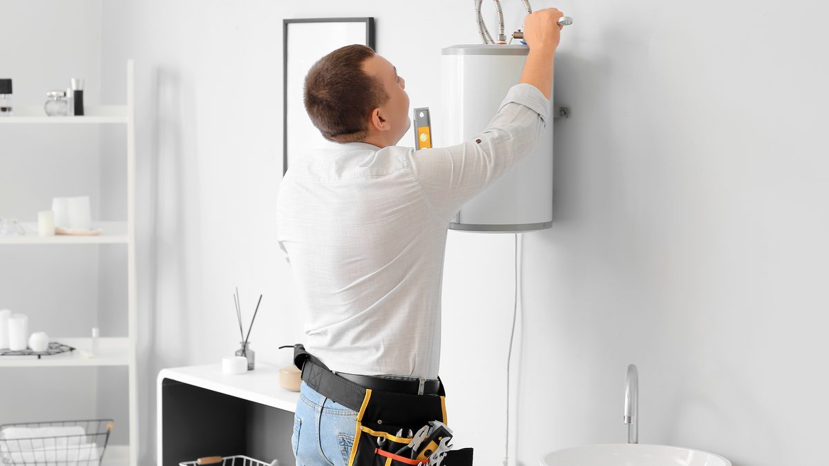 Technician working on the flexible connection at the top of a wall-mounted electric water heater